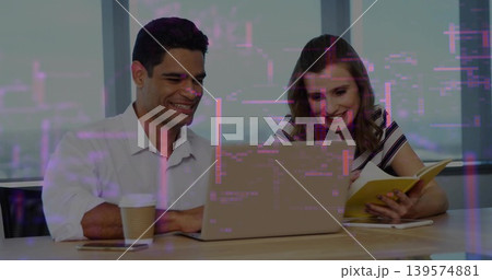 Working pair leaning over laptop at office, in white shirt and striped top, holding yellow notebook Working pair leaning over laptop at office, in white shirt and striped top, holding yellow notebook 139574881