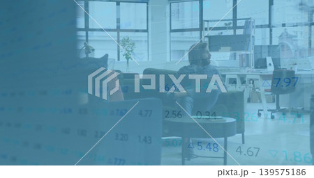 Sitting adult male in sweater, pants studying data overlay in office lounge, with sofa and monitor 139575186