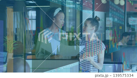 Discussing two women with headband comparing market charts on prints and tablet by glass partition Discussing two women with headband comparing market charts on prints and tablet by glass partition 139575334