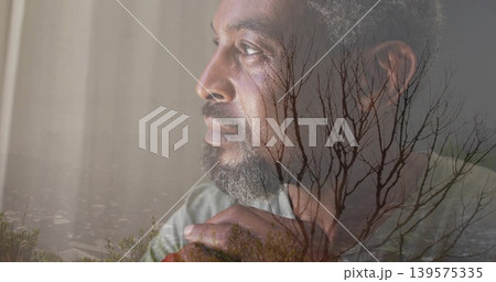 Gazing mature man wearing muted gray shirt near window, with clasped hands and branches overlay Gazing mature man wearing muted gray shirt near window, with clasped hands and branches overlay 139575335