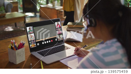 Writing girl striped tee headset at wooden table with laptop notebook on online call, copy space Writing girl striped tee headset at wooden table with laptop notebook on online call, copy space 139575459