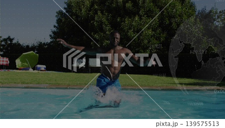 Jumping shirtless man wearing blue swim trunks splashing into backyard pool, with green umbrella 139575513