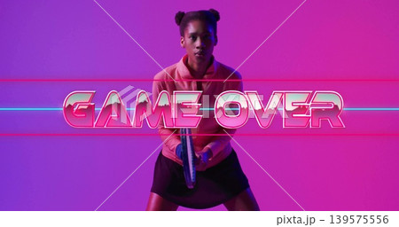 Standing woman in pink top and black skirt holding controller at studio, GAME OVER neon Standing woman in pink top and black skirt holding controller at studio, GAME OVER neon 139575556