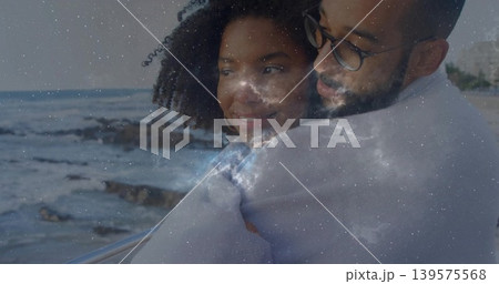 Embracing couple leaning against metal railing at seaside, wearing light sweaters, galaxy overlay Embracing couple leaning against metal railing at seaside, wearing light sweaters, galaxy overlay 139575568