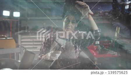 Welding woman wearing plaid top, protective apron and heavy gloves handling torch at workshop bench Welding woman wearing plaid top, protective apron and heavy gloves handling torch at workshop bench 139575625