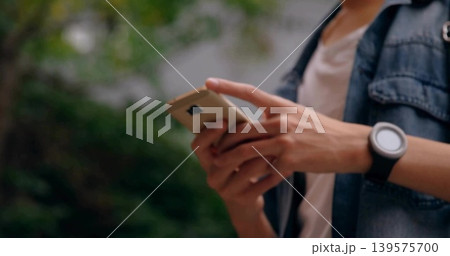 Scrolling adult male in denim jacket using smartphone with both hands in park, showing smartwatch Scrolling adult male in denim jacket using smartphone with both hands in park, showing smartwatch 139575700