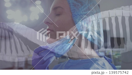Adjusting female surgeon in blue gown fixing surgical mask strap in operating room, purple gloves 139575742