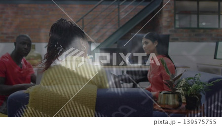 Discussing colleagues wearing yellow sweater and red tops on blue sofa in office, glass reflections Discussing colleagues wearing yellow sweater and red tops on blue sofa in office, glass reflections 139575755