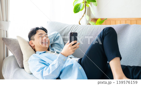 ソファに寝転んでスマートフォンを使う男性 ソファに寝転んでスマートフォンを使う男性 139576159