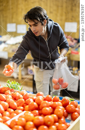 Young man chooses tomatoes in store Young man chooses tomatoes in store 139576397