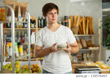 Young man store visitor chooses plastic package with salted herring, hold and view product 139576407