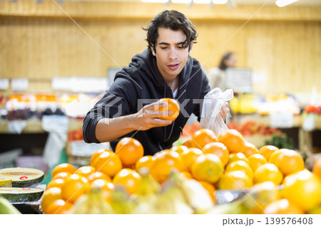 Young man chooses oranges in store Young man chooses oranges in store 139576408
