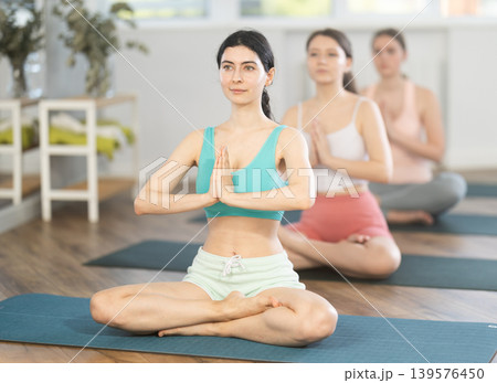 Young girl teaches yoga lesson, shows students technique of performing padmasana asana Young girl teaches yoga lesson, shows students technique of performing padmasana asana 139576450