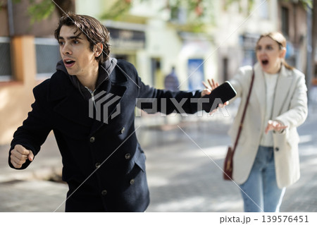 Male thief trying to snatch mobile phone of frightened woman on city Male thief trying to snatch mobile phone of frightened woman on city 139576451