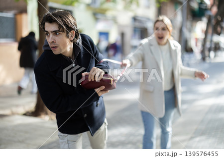 Young man snatching handbag from woman on street 139576455