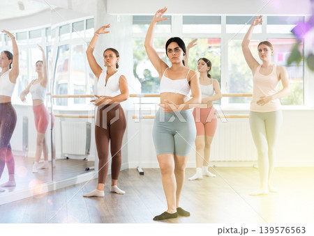 Young female ballet dancer executing dance moves with focused precision among group of people rehearsing in ballet studio Young female ballet dancer executing dance moves with focused precision among group of people rehearsing in ballet studio 139576563