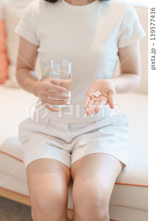 woman hand holding medicine painkiller pill and water glass on the sofa at home, taking for headaches, stomach ache, Diarrhea Pain from food poisoning, Endometriosis, Hysterectomy and Menstrual woman hand holding medicine painkiller pill and water glass on the sofa at home, taking for headaches, stomach ache, Diarrhea Pain from food poisoning, Endometriosis, Hysterectomy and Menstrual 139577436