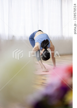 明るい窓辺のそばでマットの上でヨガのハイランジのポーズをとる日本人のミドル女性 139578514