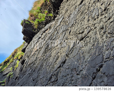 Steep rocky cliff with grass against blue sky Steep rocky cliff with grass against blue sky 139578616