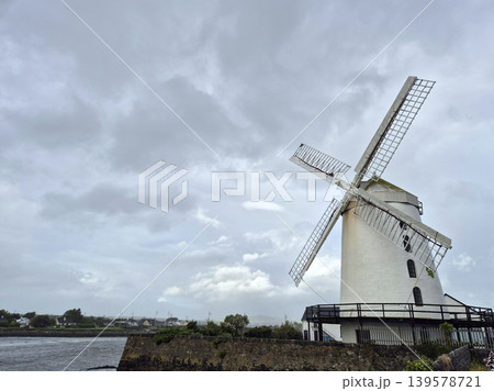 Historic windmill under cloudy sky by the water Historic windmill under cloudy sky by the water 139578721