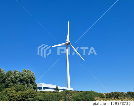 Wind turbine on clear blue sky above greenery 139578729