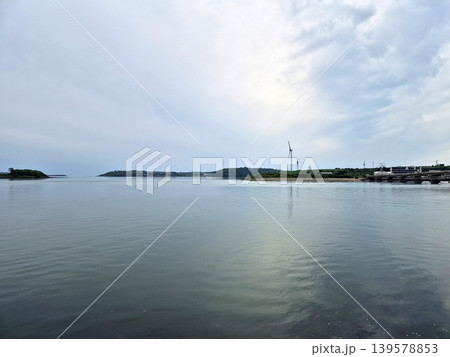 Calm coastal bay with wind turbines and cloudy sky Calm coastal bay with wind turbines and cloudy sky 139578853