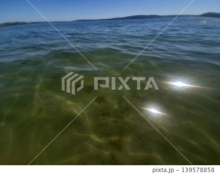 Sunlit calm sea with distant shoreline Sunlit calm sea with distant shoreline 139578858