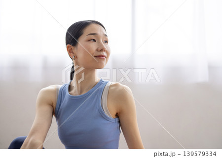明るい窓辺のそばでマットの上でヨガの半魚王のポーズをとる日本人のミドル女性 139579334