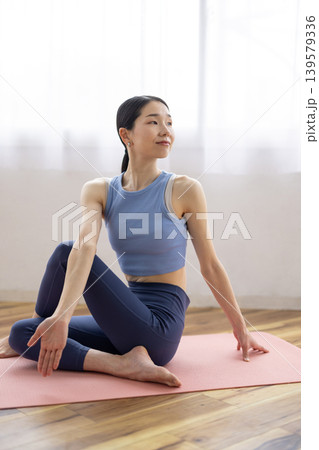 明るい窓辺のそばでマットの上でヨガの半魚王のポーズをとる日本人のミドル女性 139579336