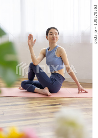 明るい窓辺のそばでマットの上でヨガの半魚王のポーズをとる日本人のミドル女性 139579363