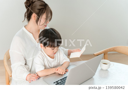 子供を抱っこしながらパソコンと貯金通帳を見るシングルマザーの女性 139580042