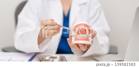 Dentist with Orthodontic tooth model and bracket or brace. Clean and Scrape off tartar. May Orthodontic Health Day, March Oral health, Dentist Day, False Teeth. Toothache and Children Dental Health 139581583
