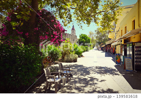 Beautiful narrow cobblestone street in the medieval Old Town of Rhodes, Greece. Historic architecture and charming atmosphere of a popular European travel destination. Beautiful narrow cobblestone street in the medieval Old Town of Rhodes, Greece. Historic architecture and charming atmosphere of a popular European travel destination. 139581618