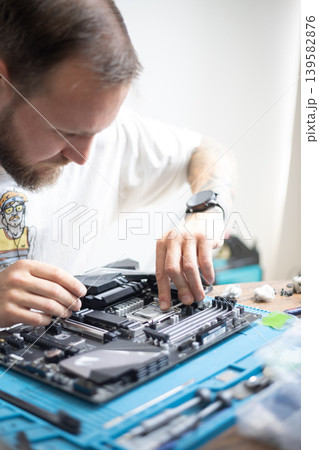Man works on computer motherboard in workshop during daylight hours 139582876