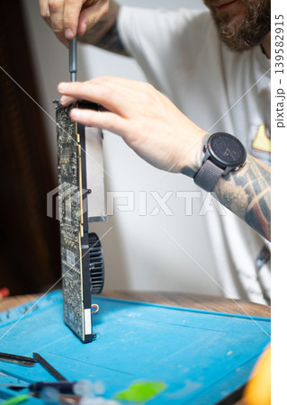 Person repairs a computer graphics card on a table in a home setting during the day 139582915