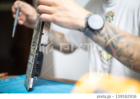 Man works on a computer graphic card repair at home with tools in early morning light 139582916