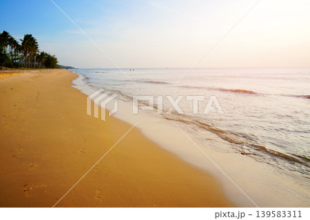 SGentle waves lap at ocean shore. Sunrise over sea beach with footprints on sand and calm water  139583311