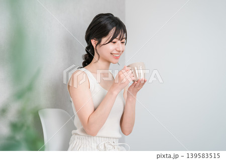 マグカップでホットドリンクを飲み温活するタンクトップ姿の若いアジア人女性の横顔 139583515