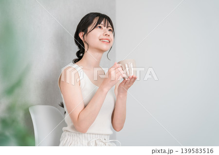 マグカップでホットドリンクを飲み温活するタンクトップ姿の若いアジア人女性の横顔 マグカップでホットドリンクを飲み温活するタンクトップ姿の若いアジア人女性の横顔 139583516