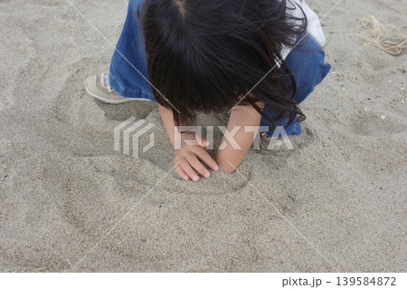 海岸の砂浜で腕を埋めて砂遊びをする子供 139584872