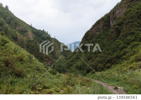 Mountain valley trail in Altai with green slopes and cloudy summer sky Mountain valley trail in Altai with green slopes and cloudy summer sky 139586561