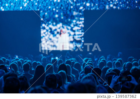 Audience watching live concert on stage with singer under blue lights and large video screen Audience watching live concert on stage with singer under blue lights and large video screen 139587362