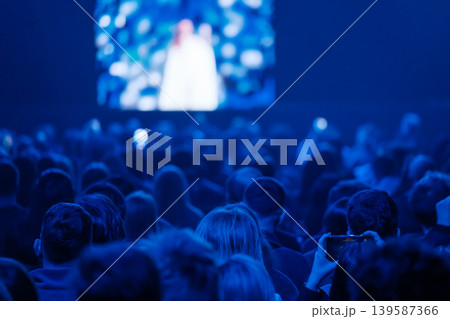 Audience watching live performance on big screen in blue lit theater crowd recording moment Audience watching live performance on big screen in blue lit theater crowd recording moment 139587366