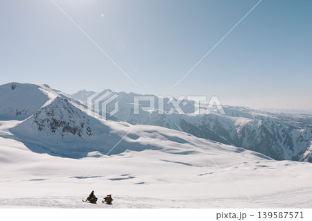 Snowmobile riders in Karakol ski base with snowy Tien Shan mountains, Kyrgyzstan Snowmobile riders in Karakol ski base with snowy Tien Shan mountains, Kyrgyzstan 139587571