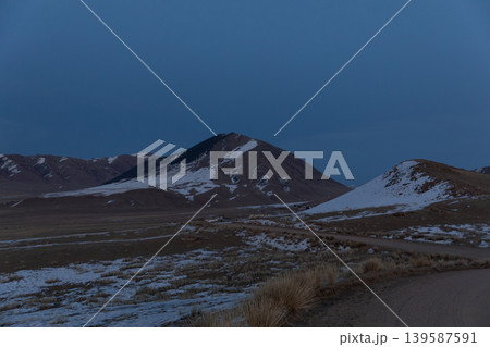 Remote mountain road at dusk in Kyrgyzstan with snowy hills and open steppe 139587591