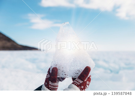 Hands holding clear ice block on frozen Lake Baikal in winter sunlight, Russia Hands holding clear ice block on frozen Lake Baikal in winter sunlight, Russia 139587848