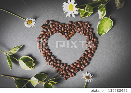Cafes and restaurants. A mug of invigorating, black coffee and coffee beans in the shape of a heart on a dark gray background. Copy space for text. The concept of hot drinks and love. Cafes and restaurants. A mug of invigorating, black coffee and coffee beans in the shape of a heart on a dark gray background. Copy space for text. The concept of hot drinks and love. 139588421