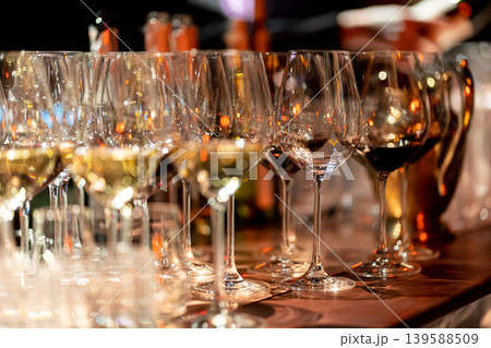 Elegant scene of wine being poured into glasses aligned in a row, showcasing the rich colors and graceful flow of the liquid, set against a dark, warm background, ideal sophisticated dining settings Elegant scene of wine being poured into glasses aligned in a row, showcasing the rich colors and graceful flow of the liquid, set against a dark, warm background, ideal sophisticated dining settings 139588509