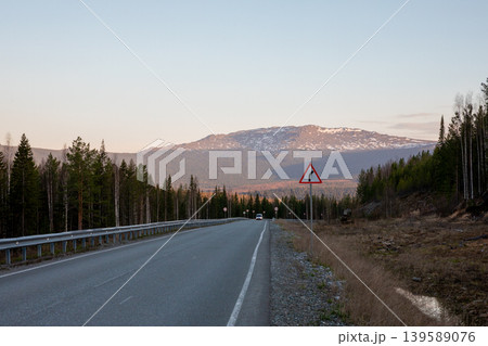 Empty highway through Ural Mountains taiga forest with snowy ridge at sunset Empty highway through Ural Mountains taiga forest with snowy ridge at sunset 139589076