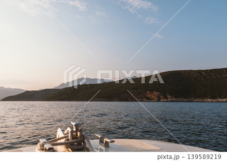 Boat bow view on calm sea near coastal mountains at golden hour light Boat bow view on calm sea near coastal mountains at golden hour light 139589219